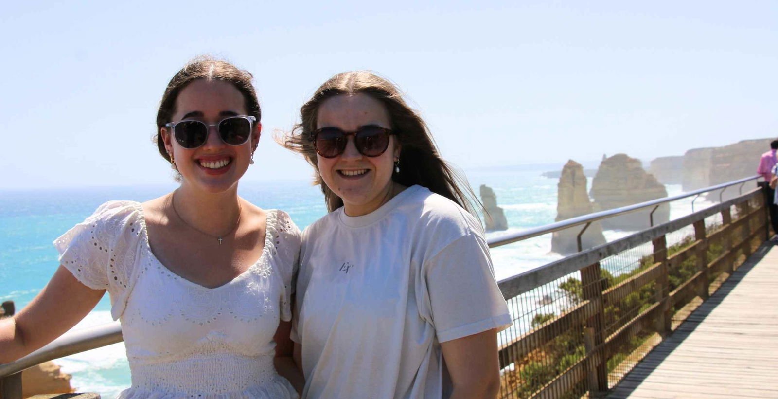 Two women stadning close together, posing for picture infront of the 12 Apostles.