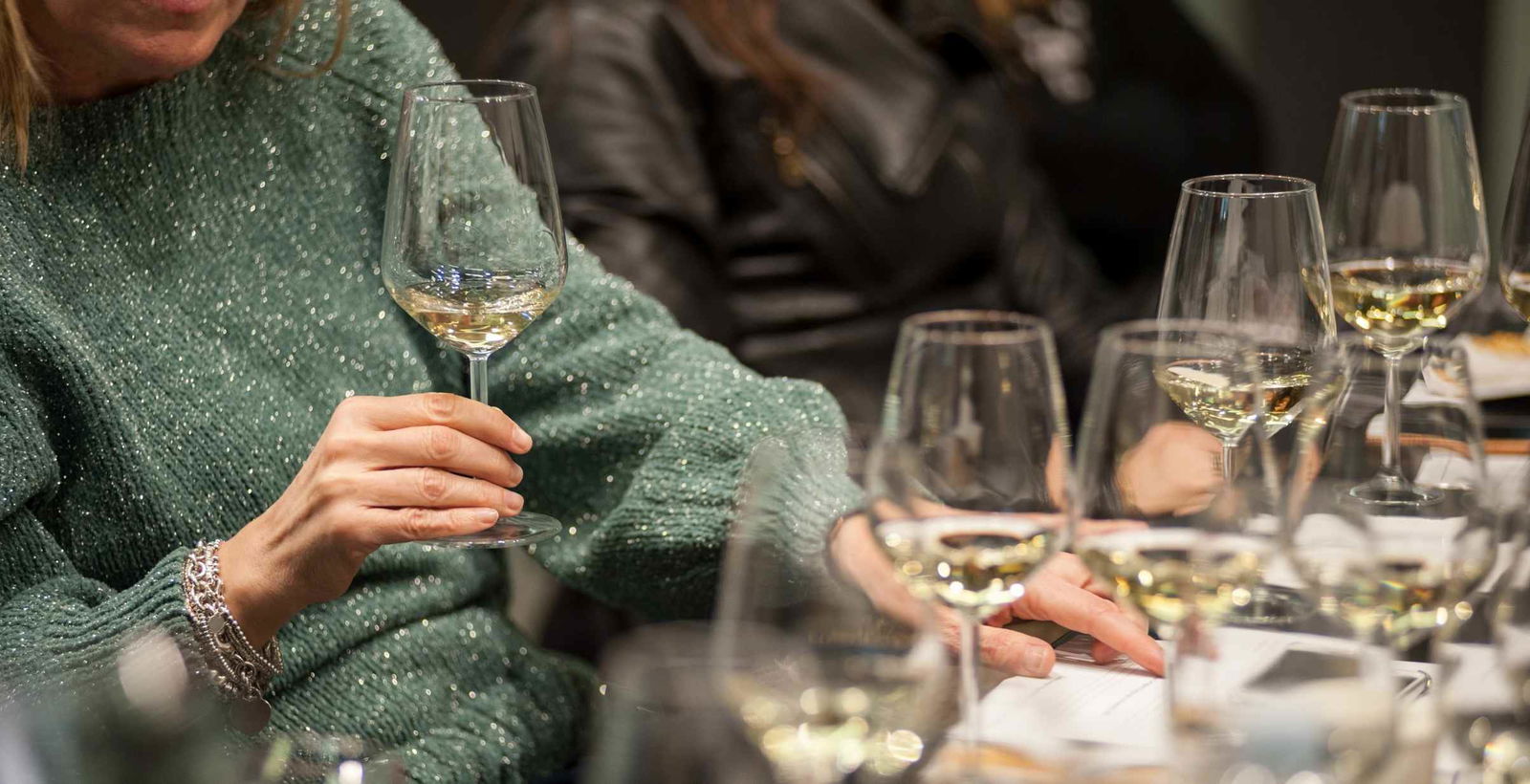 A woman holding a wine glass sitting at a table with many wine tasting glasses around.
