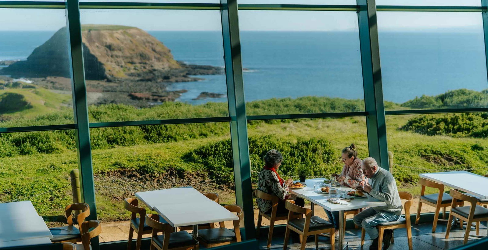 People eating lunch at cafe in the Nobbies Center in front of big glass windows on Phillip Island.