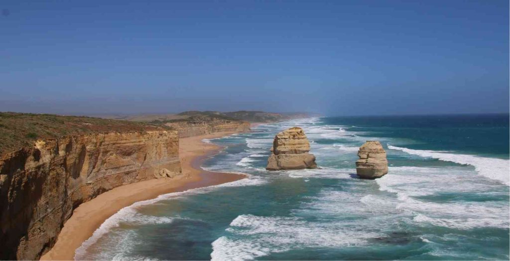 Large sandstone rock formations jutting out from the crashing waves of the ocean sperated from the large talls cliffs that line the Great Ocean Road.