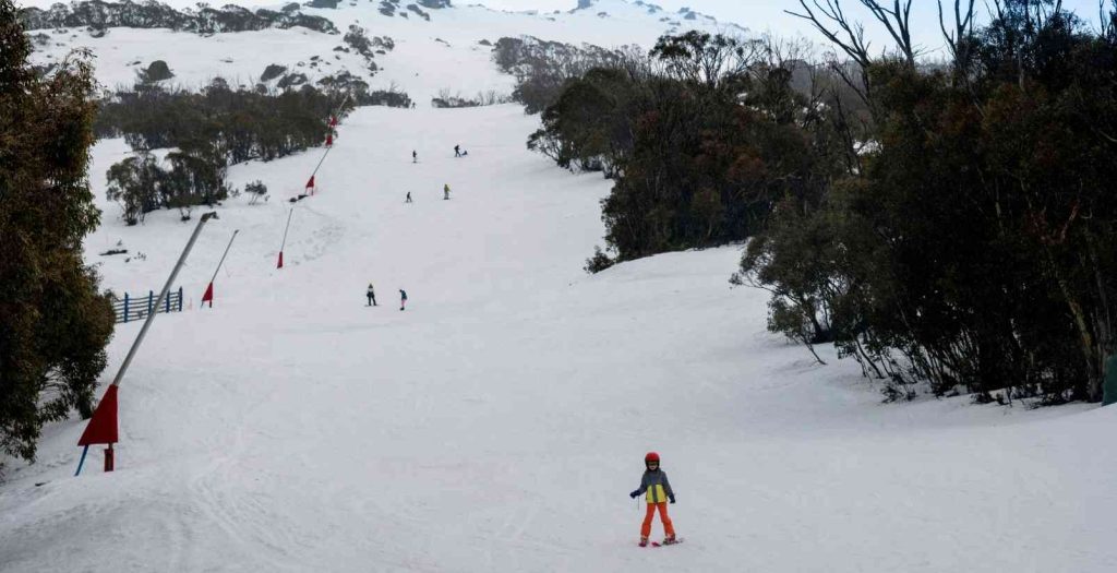 People and children skiing and snowboarding down a snowy mountains at Mt Buller on a cold, foggy winters day.