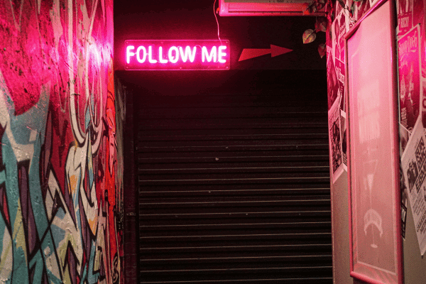 Neon pink light up sign that says follow me with stairs in the background
